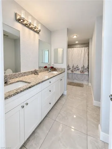Double vanity with light-toned stone countertops, undermount sinks, white cabinetry, and large-format tile flooring