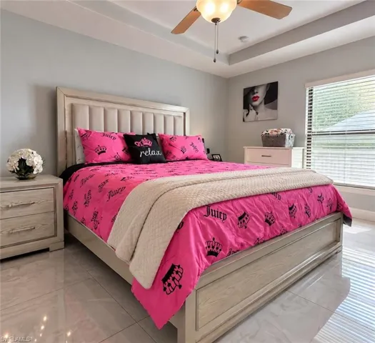 Bedroom featuring a tray ceiling, ceiling fan with integrated lighting, window with horizontal blinds, and large-format tile flooring