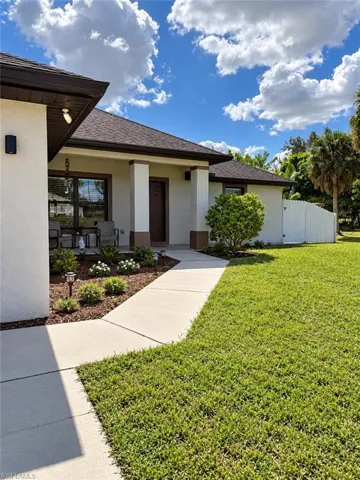 Stucco exterior with covered entryway, concrete walkway, and white vinyl perimeter fencing