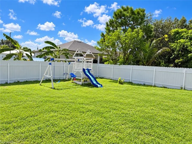 Expansive backyard featuring a manicured lawn, white vinyl perimeter fencing, and mature trees