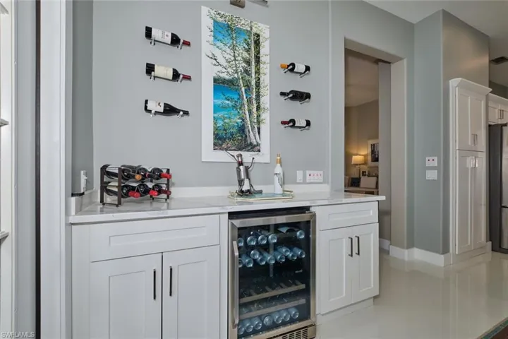 Bar with stainless steel refrigerator, white cabinetry, beverage cooler, light stone counters, and light tile patterned floors