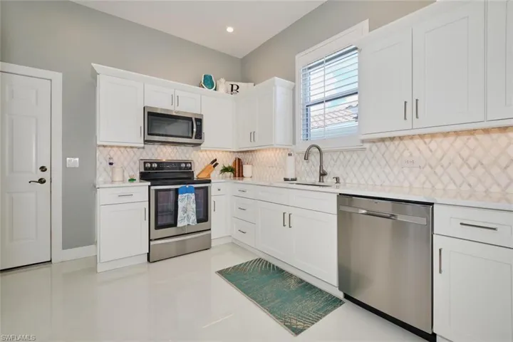 Kitchen with white cabinets, appliances with stainless steel finishes, decorative backsplash, and sink