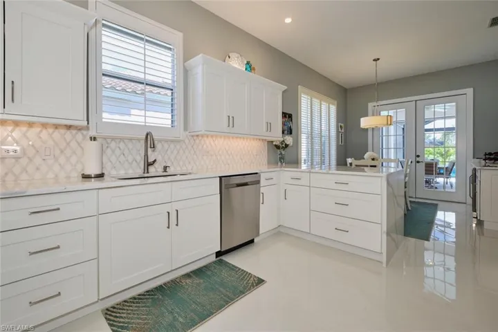Kitchen with french doors, sink, stainless steel dishwasher, decorative light fixtures, and kitchen peninsula