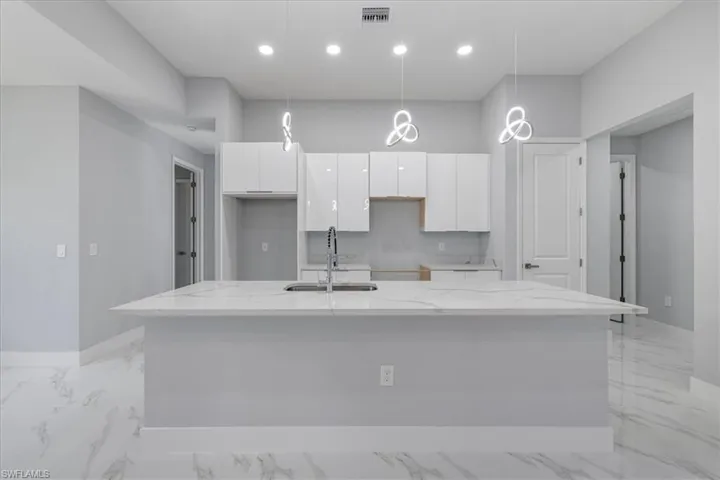 Kitchen with pendant lighting, a kitchen island with sink, sink, light stone counters, and white cabinetry