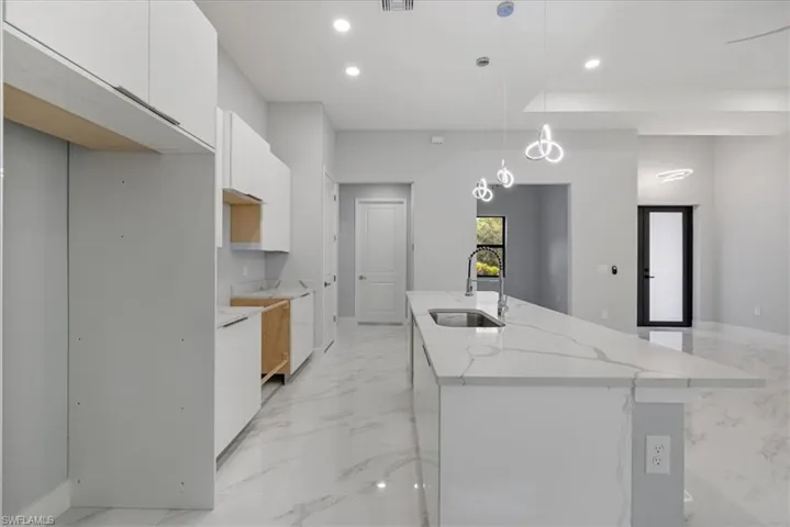 Kitchen with light stone countertops, sink, an island with sink, decorative light fixtures, and white cabinets