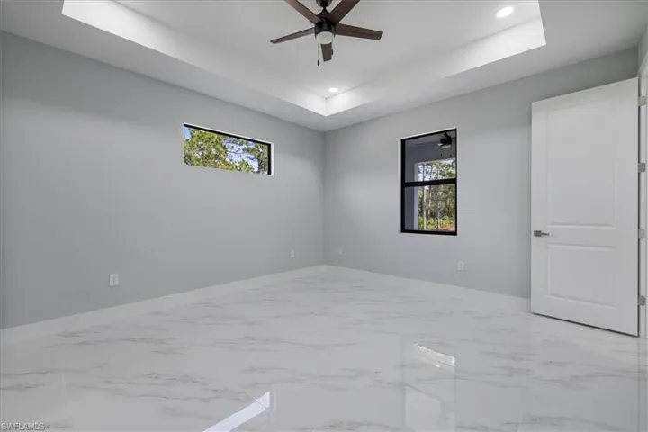 Empty room with a tray ceiling, plenty of natural light, and ceiling fan