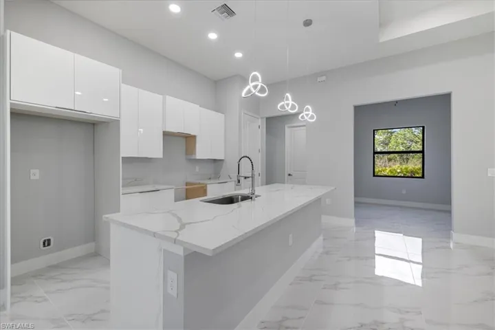 Kitchen with light stone countertops, white cabinetry, sink, an island with sink, and pendant lighting
