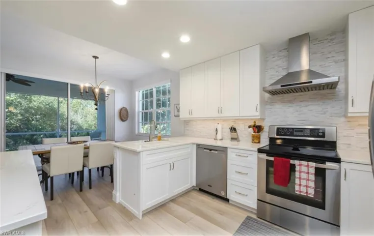 Kitchen with appliances with stainless steel finishes, wall chimney exhaust hood, white cabinets, a peninsula, and recessed lighting