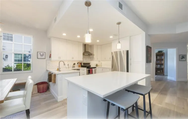 Kitchen featuring a kitchen bar, stainless steel appliances, white cabinets, pendant lighting, and wall chimney exhaust hood