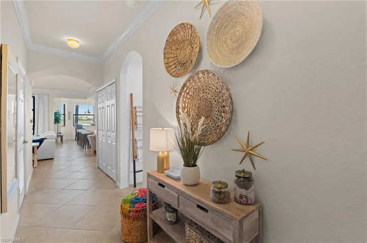 Hall featuring a textured wall, arched walkways, crown molding, and light tile patterned floors