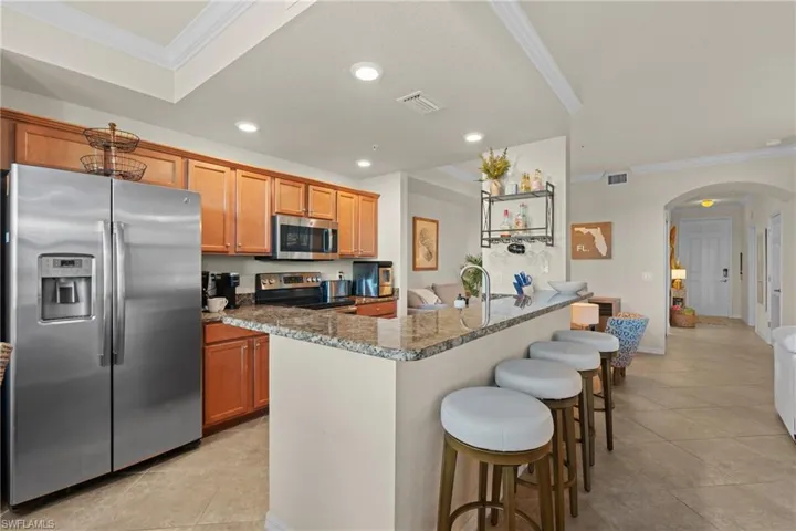 Kitchen with arched walkways, appliances with stainless steel finishes, an island with sink, and light stone countertops