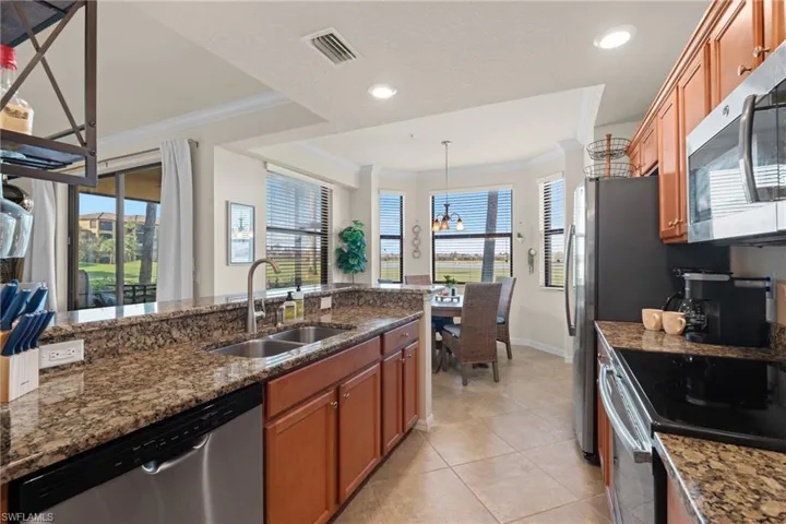 Kitchen with dark stone counters, appliances with stainless steel finishes, crown molding, pendant lighting, and a sink