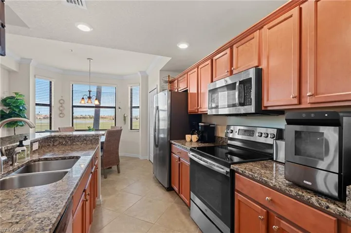 Kitchen with dark stone counters, ornamental molding, decorative light fixtures, stainless steel appliances, and a sink
