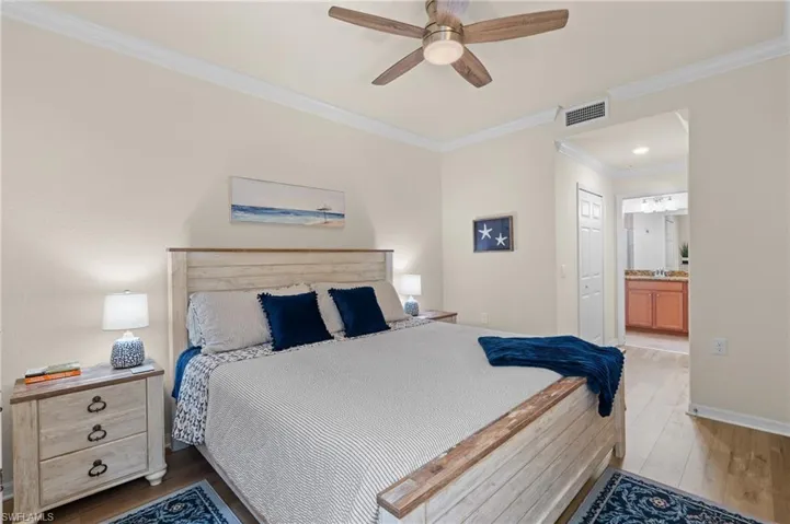 Bedroom with visible vents, light wood-style flooring, ensuite bathroom, ornamental molding, and baseboards