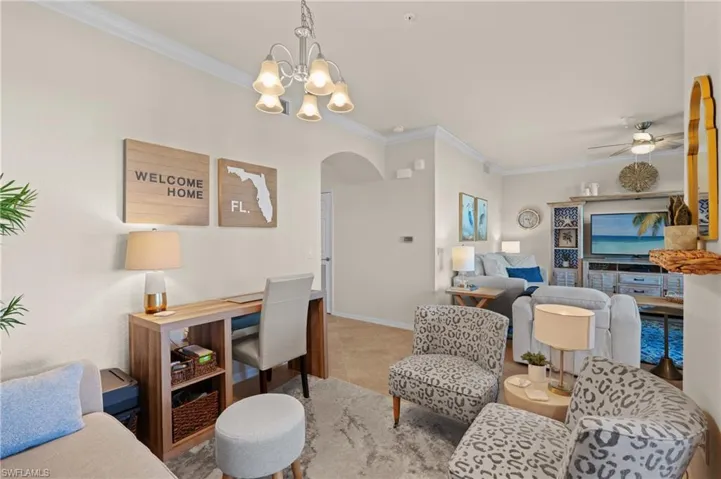 Living room with arched walkways, light tile patterned floors, ornamental molding, baseboards, and ceiling fan with notable chandelier
