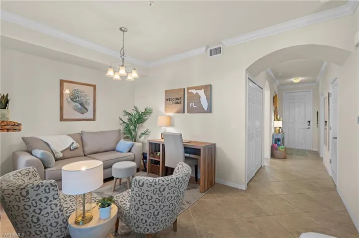 Living room featuring arched walkways, light tile patterned floors, visible vents, baseboards, and crown molding