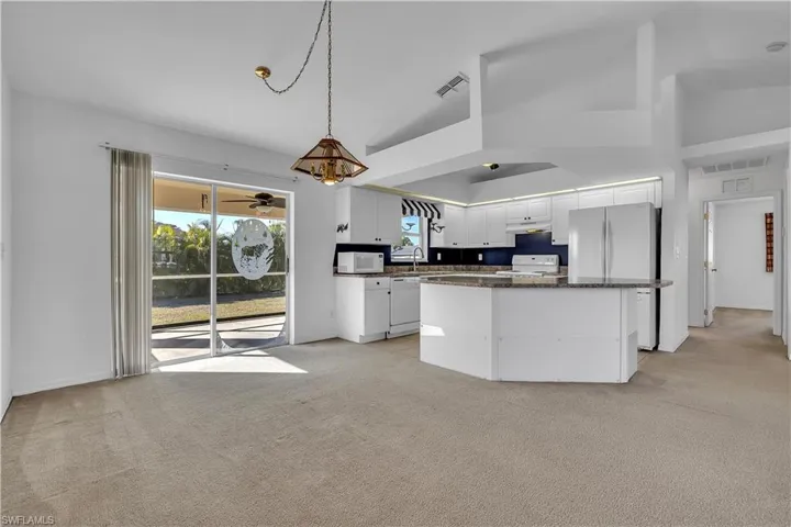 Kitchen with white cabinets, light carpet, white appliances, dark stone counters, and lofted ceiling