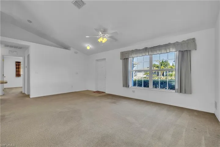 Spare room featuring a ceiling fan, light carpet, and vaulted ceiling