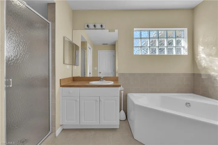 Full bathroom featuring a garden tub, a stall shower, vanity, and light tile patterned floors