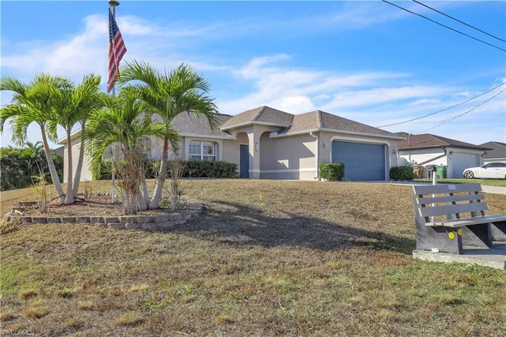 Ranch-style home with stucco siding, a front yard, an attached garage, and roof with shingles
