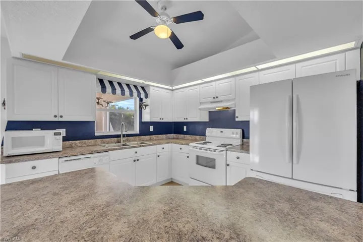 Kitchen featuring white appliances, white cabinetry, and ceiling fan