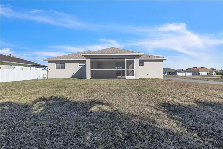 Rear view of house with a sunroom, stucco siding, a yard, and roof with shingles