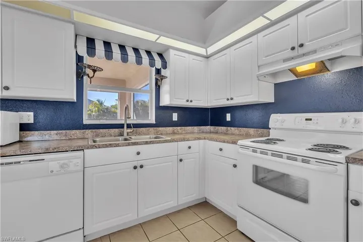 Kitchen with white appliances, a textured wall, white cabinetry, and light tile patterned floors
