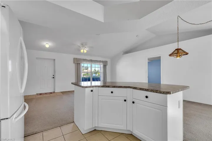 Kitchen with freestanding refrigerator, light colored carpet, dark countertops, white cabinetry, and a center island