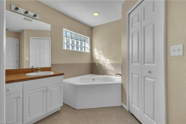 Full bathroom with a closet, a garden tub, vanity, a textured wall, and light tile patterned flooring