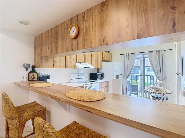 The kitchen features a breakfast bar with two bar stools, wooden cabinetry, and white appliances