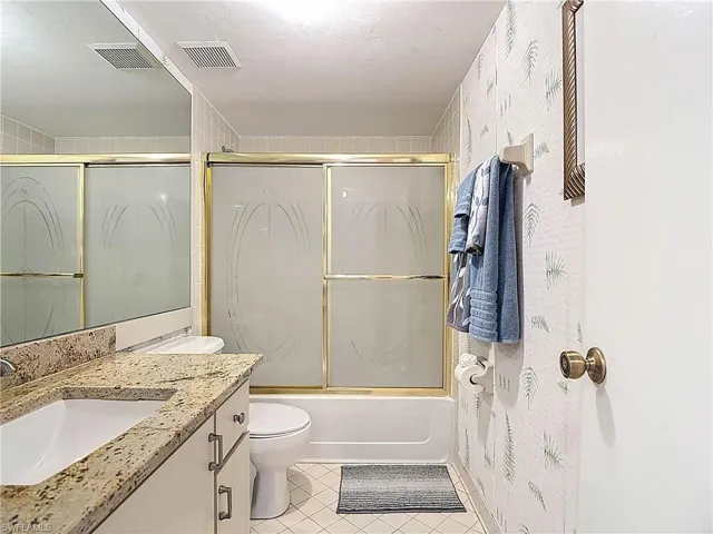 Bathroom featuring a vanity with a granite countertop and an integrated sink, a mirror, and a shower with sliding doors