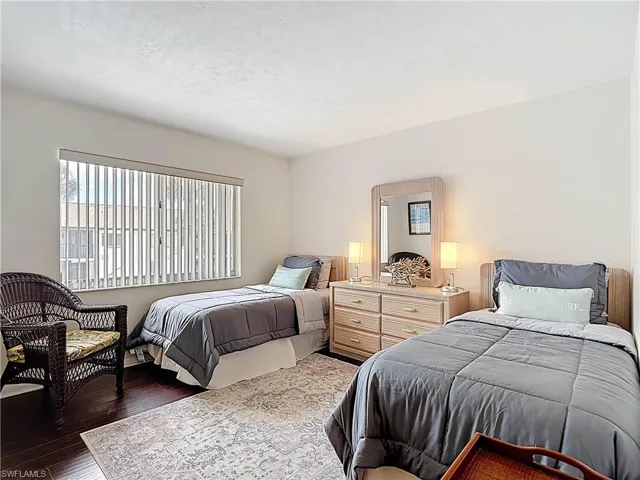 Bedroom featuring dark wood flooring, a window with vertical blinds, and light-colored walls