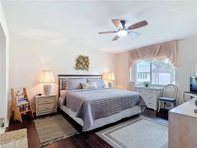 The property features dark wood flooring, a ceiling fan with integrated lighting, and a large window with draped window treatments