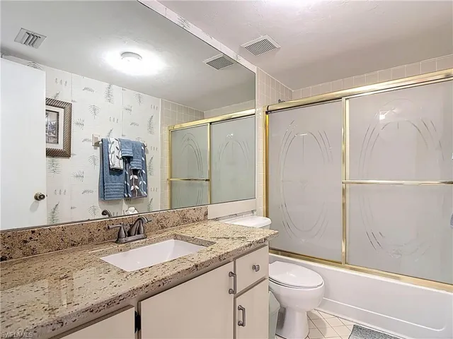The bathroom features a vanity with a granite countertop and an integrated sink, a large mirror, and a shower with frosted sliding glass doors