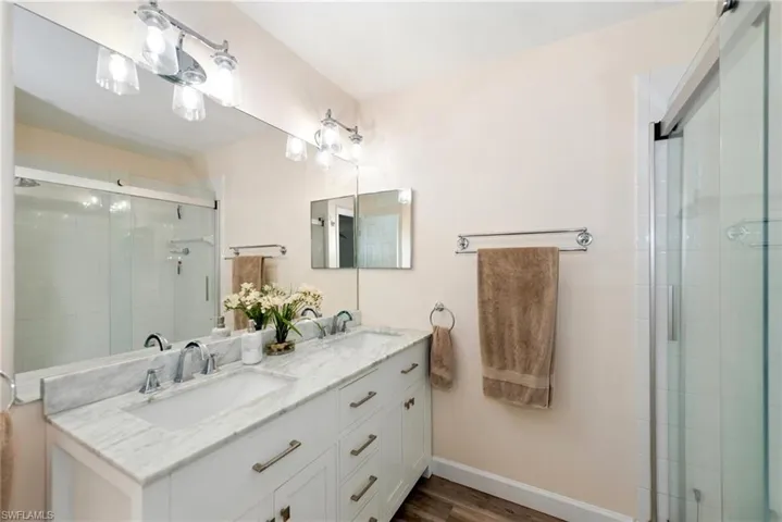 Bathroom with double vanity, a stall shower, and dark wood finished floors