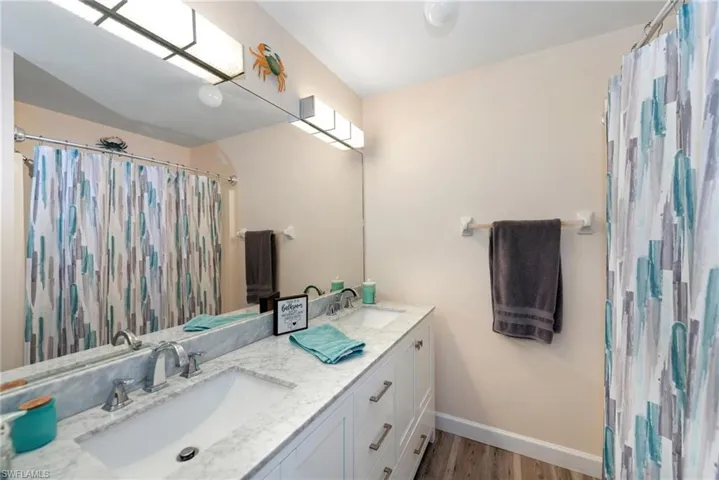 Full bathroom with double vanity, a shower with shower curtain, and light wood-style floors