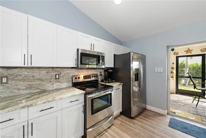 Kitchen featuring stainless steel appliances, vaulted ceiling, white cabinets, light stone countertops, and backsplash