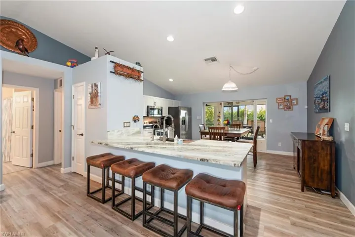 Kitchen featuring vaulted ceiling, a kitchen bar, a peninsula, light wood-style flooring, and stainless steel appliances