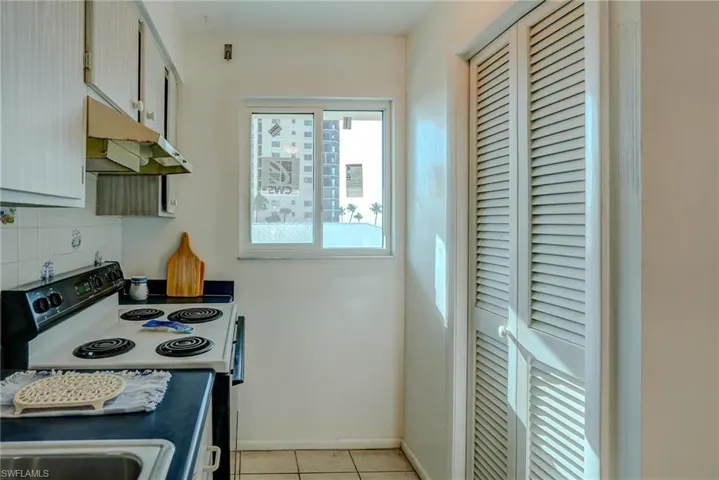 Kitchen with electric range oven, under cabinet range hood, light tile patterned floors, backsplash, and dark countertops