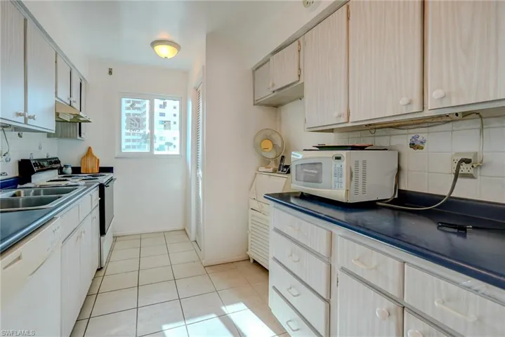 Kitchen with decorative backsplash, white appliances, dark countertops, light tile patterned floors, and under cabinet range hood