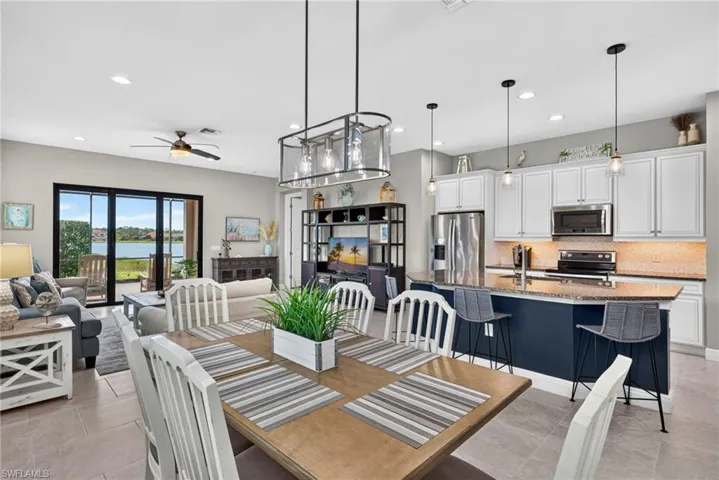 Open-concept kitchen and dining area featuring a multi-tone island, stone-surfaced countertops, white shaker-style cabinetry, stainless steel appliances, and tile flooring