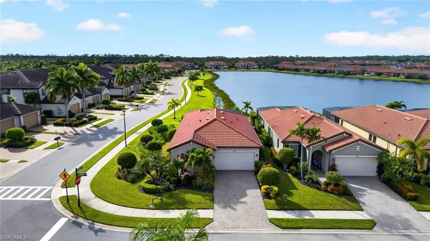 Aerial perspective of a residential street featuring tile-roof architecture, paver driveways, manicured lawns, and waterfront exposure