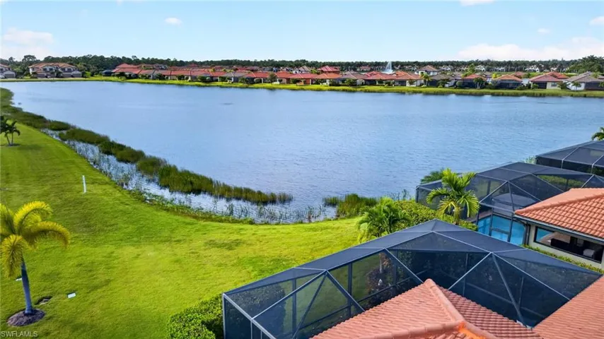 Waterfront property featuring an extended screened-in lanai, tile roof, and expansive lawn
