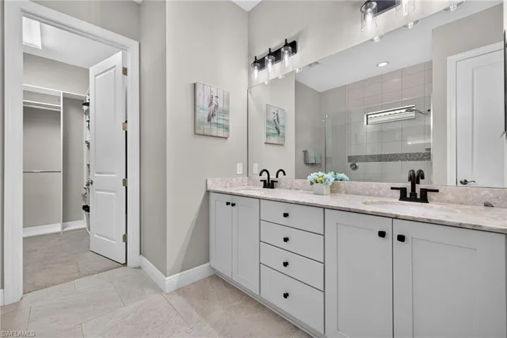 rimary bathroom with double vanity featuring shaker-style cabinetry, quartz countertops, an enclosed glass walk-in shower, and a walk-in closet