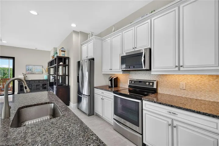Kitchen featuring shaker-style white cabinetry, stone countertops, stainless steel appliances, a tiled backsplash, and a central island with an undermount sink