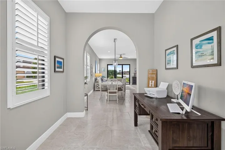 Interior foyer/entry featuring an arched entryway, neutral-toned tile flooring, and shutter-style window coverings