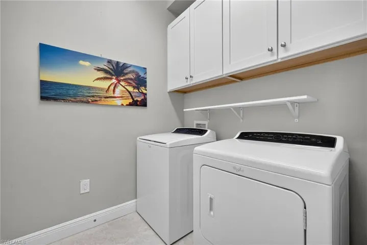 Laundry space featuring white shaker-style wall-mounted cabinetry, a fixed open shelving unit, and light-toned tile flooring