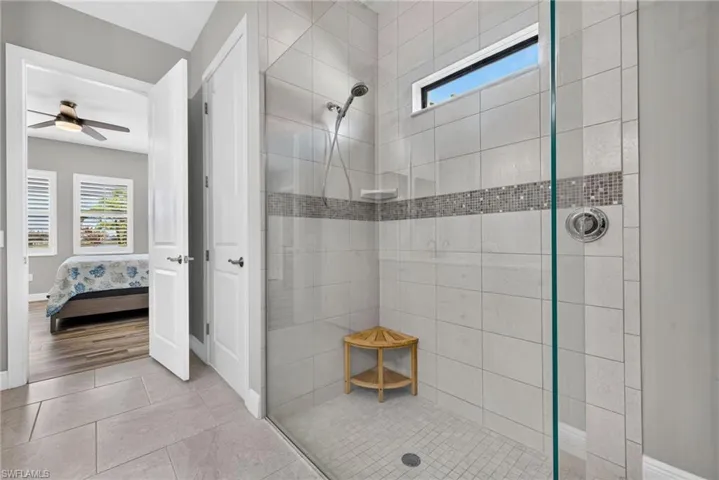 Walk-in shower featuring large-format ceramic wall tile, a decorative mosaic tile inlay, a glass enclosure, a built-in corner shelf, and a rain-style showerhead