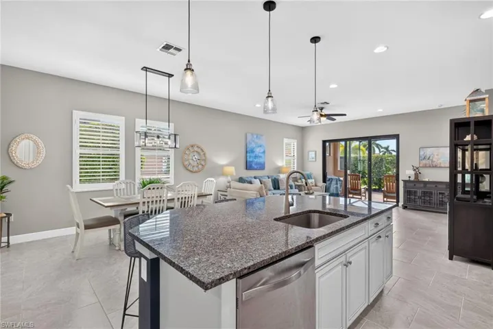 Kitchen featuring a stone-topped island with an integrated stainless steel sink, tile flooring, pendant lighting, and plantation shutters