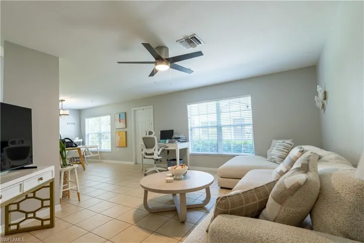 Living room with a desk, light tile patterned floors, and a ceiling fan